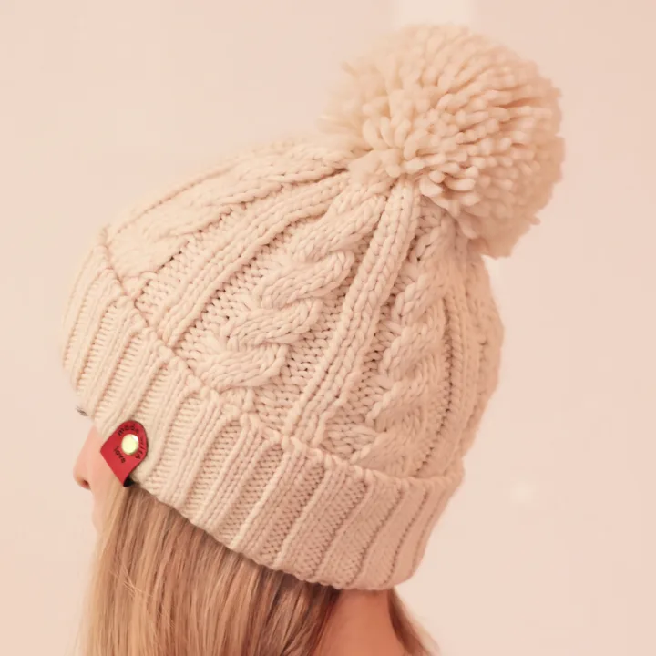 Cream hat with a pom-pom, cable knit and a leather patch