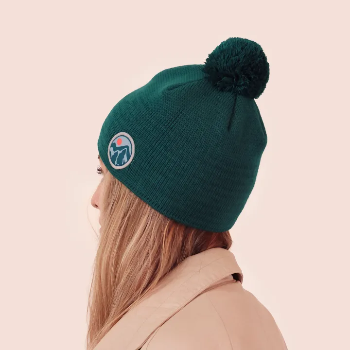 Bottle-green hat with a pom-pom and a round patch with a mountain motif