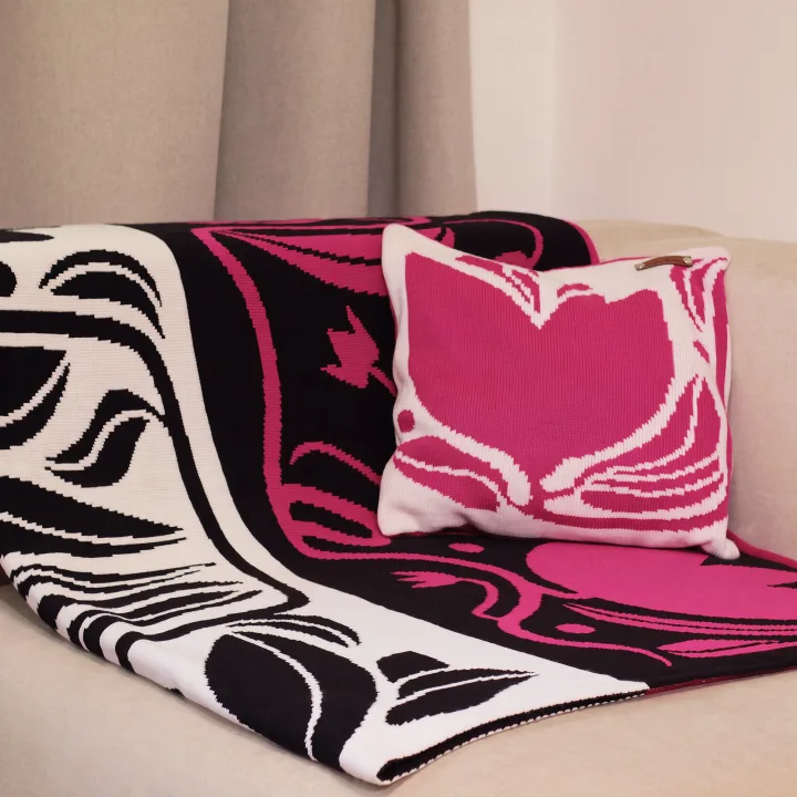 Black and pink dothat blanket with a floral pattern and a tulip pillow on a sofa
