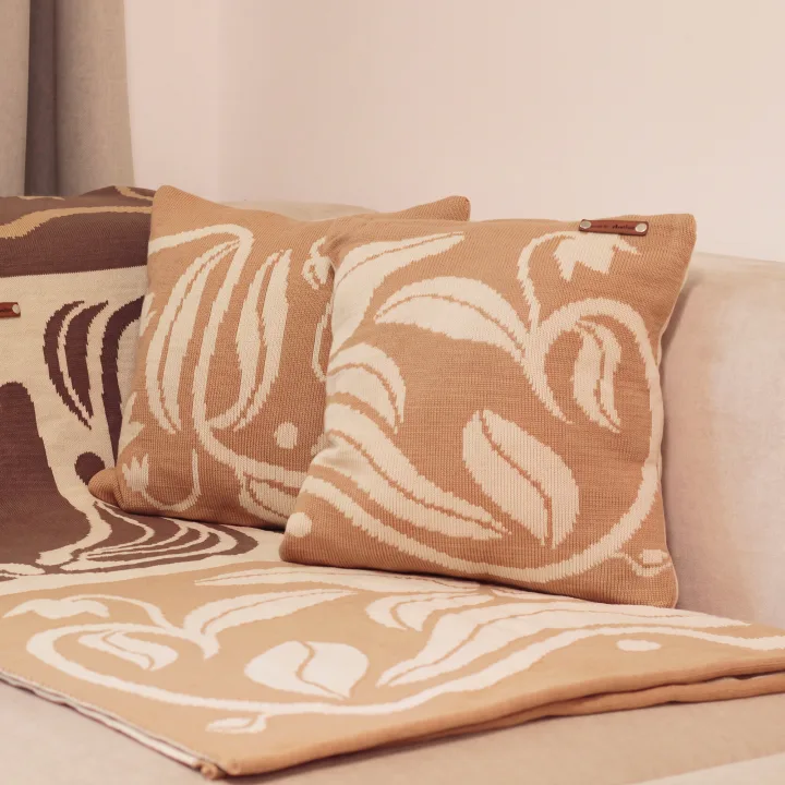 Caramel dothat pillows with a cream leaf motif on a sofa, on a blanket in the same pattern