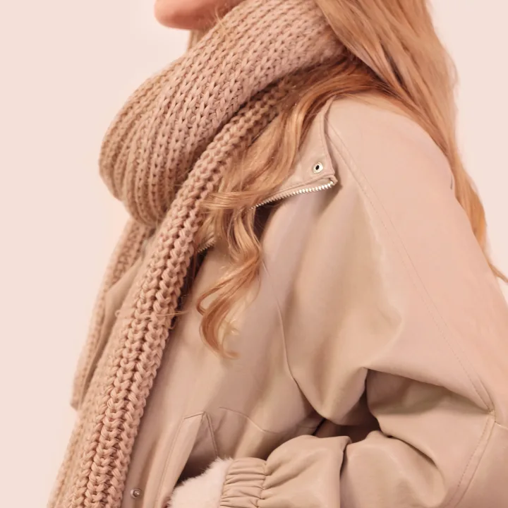 Beige chunky-knit scarf thrown over the shoulder of a light jacket